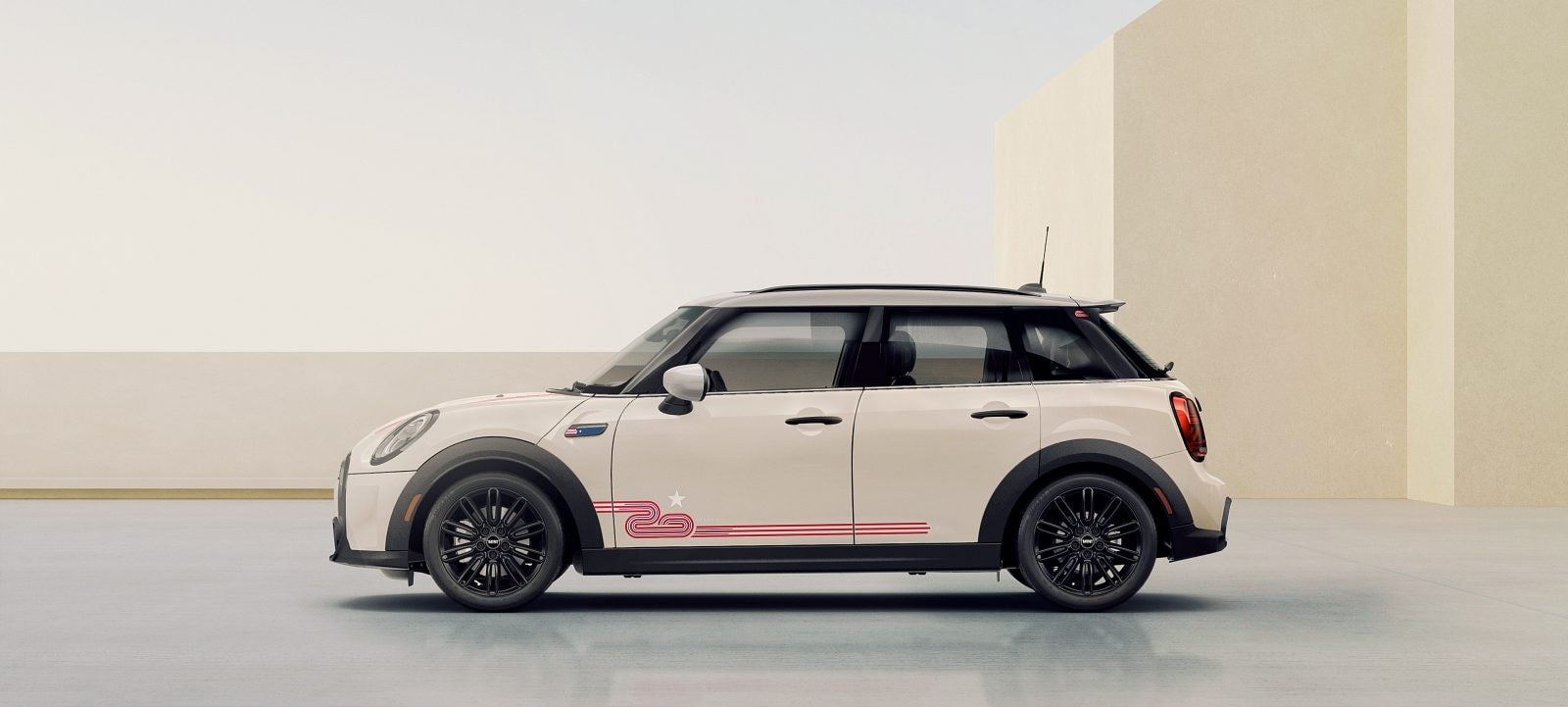 Side view of a MINI 20 Years Edition in Pepper White facing left, parked on a grey surface with beige rectangular buildings and a clear sky in the background. | MINI of Sterling in Sterling VA