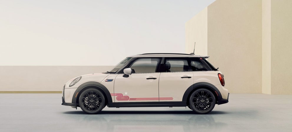 Side view of a MINI 20 Years Edition in Pepper White facing left, parked on a grey surface with beige rectangular buildings and a clear sky in the background. | MINI of Sterling in Sterling VA