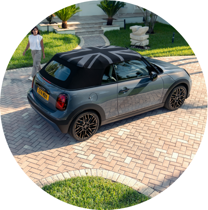 Bird’s-eye view of a MINI Cooper Convertible with a Union Jack soft top roof parked on a stone driveway with the driver walking towards it.