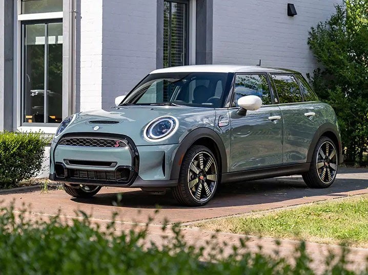 Three-quarters front view of a MINI Hardtop 4 Door Multitone Edition in Sage Green parked in front of a white building.