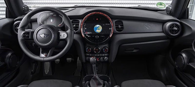 Closeup view of the front row of a MINI John Cooper Works 1to6 Edition vehicle from the perspective of the back row, with a metal wall and metal fencing visible through the windshield in the background.